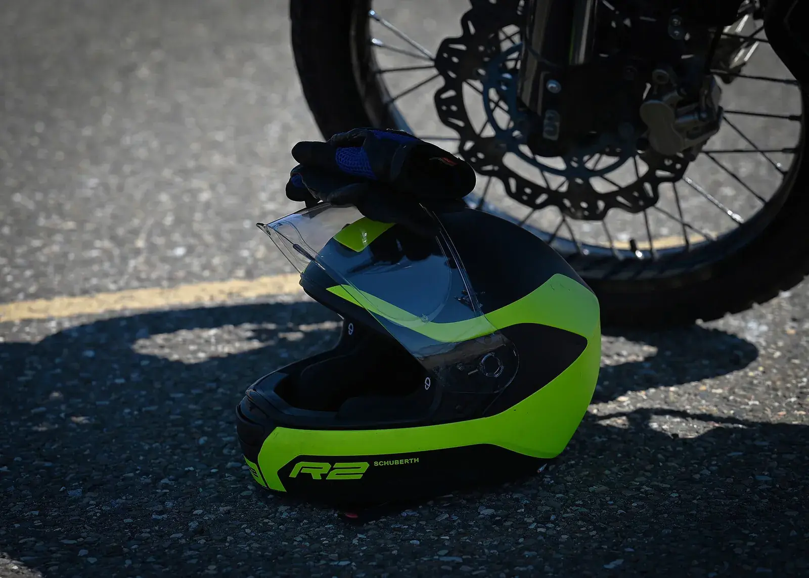 Een motorhelm met handschoenen op het asfalt naast het voorwiel van een motor.